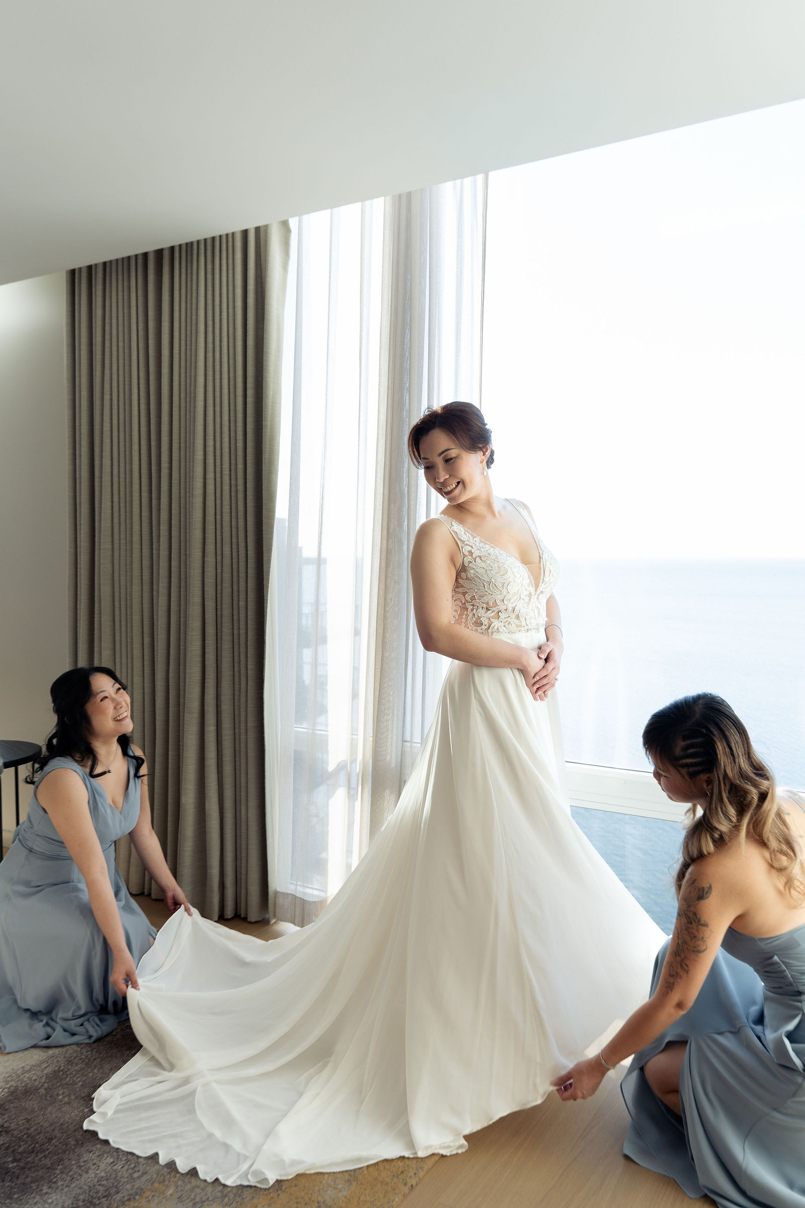 Bridesmaids arrange gown by lake window